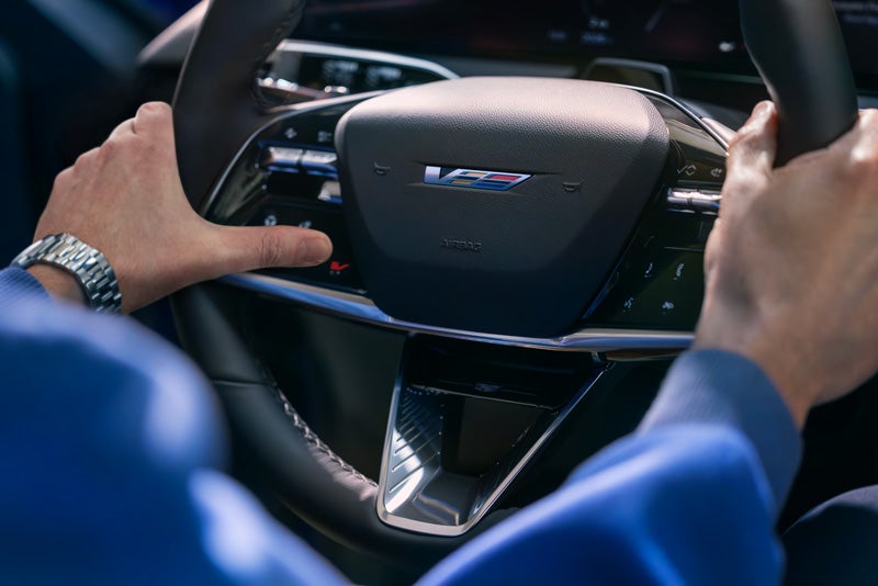 Close-up of a Man About to Press the V-Button on the 2026 OPTIQ-V Steering Wheel | Cadillac of Marion in Marion IL